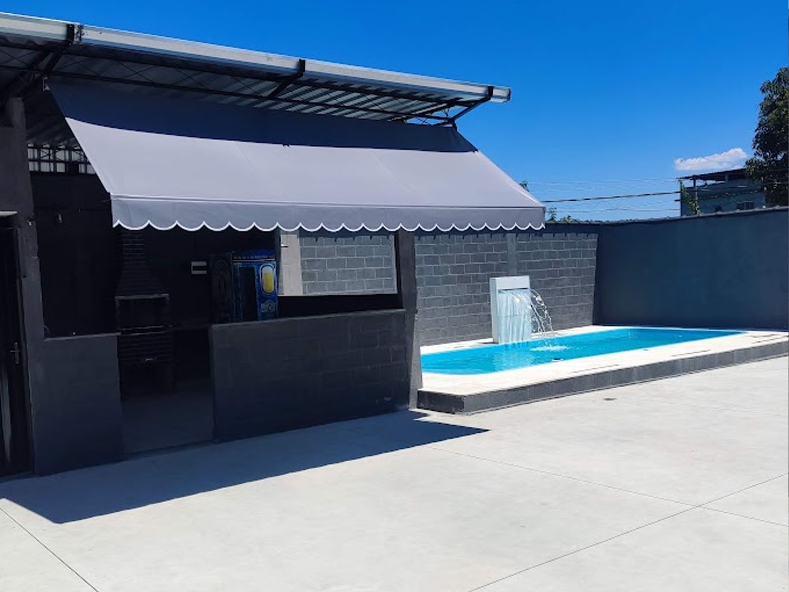Área da churrasqueira com toldo ao lado da piscina, na Vila Maia
