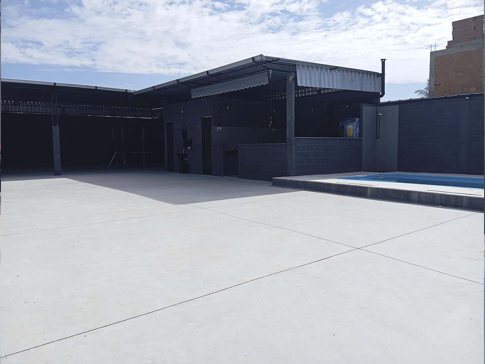 Salão aberto com piso de concreto e piscina ao fundo